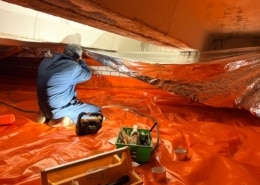 Monteur die isolatiemateriaal plaatst in een kruipruimte met oranje folie op de vloer en reflecterend materiaal aan het plafond