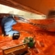 Monteur die isolatiemateriaal plaatst in een kruipruimte met oranje folie op de vloer en reflecterend materiaal aan het plafond